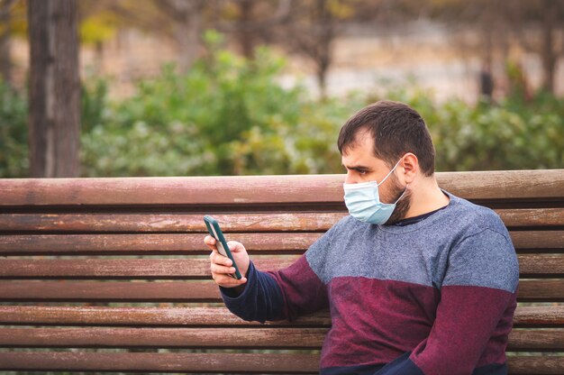 Ragazzo con maschera protettiva che si fa un selfie su una panchina del parco al tramonto