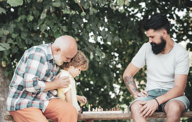 Ragazzo con padre e nonno godendo insieme nel parco Vecchio con ragazzino che gioca a scacchi
