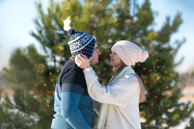 Ragazzo con un bacio ragazza su uno sfondo di albero di Natale verde decorato con festosi giocattoli e ghirlande in inverno nella foresta