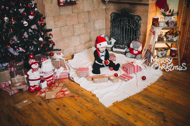 ragazzo con un cappello di Babbo Natale all'arredamento di Natale in vacanza tiene una palla giocattolo sull'albero di Natale