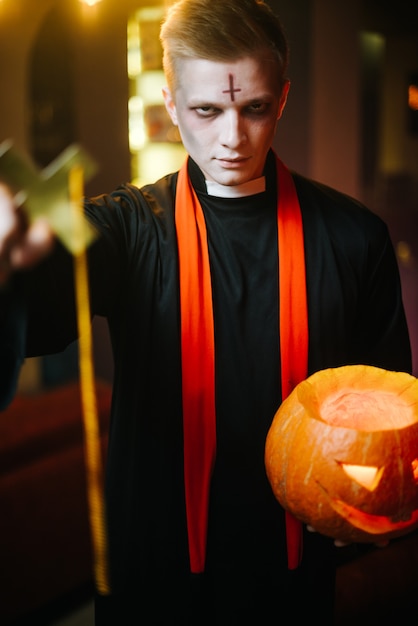 Ragazzo con un costume da prete di Halloween che tiene in mano una zucca intagliata