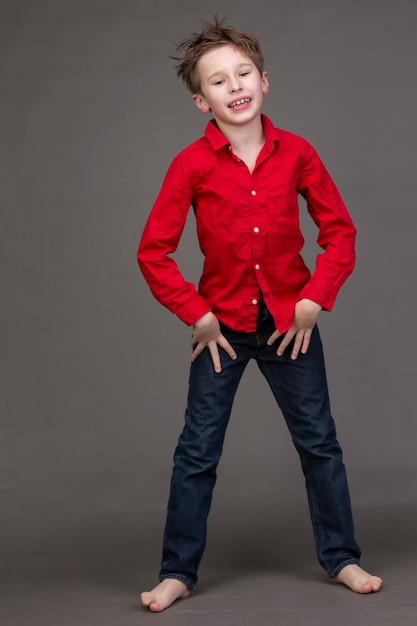 ragazzo con una camicia rossa e jeans su uno sfondo grigio Un bambino nel mondo della moda sta posando