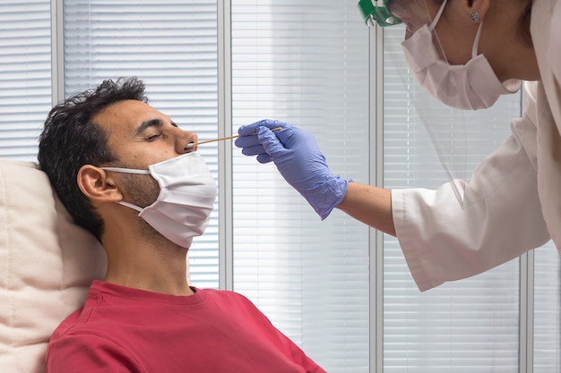 Ragazzo con una maglietta rossa e una maschera seduto mentre un'infermiera con protezione anti-covid-19 esegue il test PCR