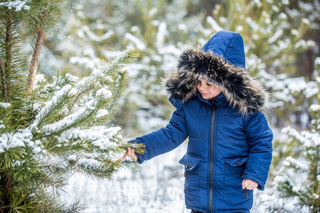 Ragazzo con una pelliccia con cappuccio cappotto invernale nella foresta invernale Ragazzo preadolescente che si diverte a giocare