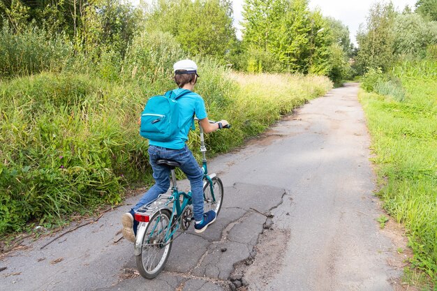 Ragazzo con zaino in bici su strada di campagna con alberi verdi dal retro