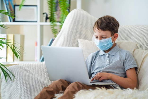 Ragazzo concentrato nella maschera con un computer portatile durante la quarantena.