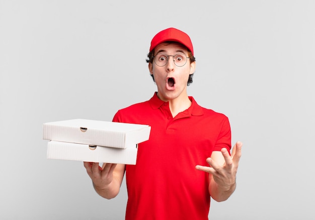 Ragazzo consegna pizza a bocca aperta e stupito, sbalordito e stupito da un'incredibile sorpresa