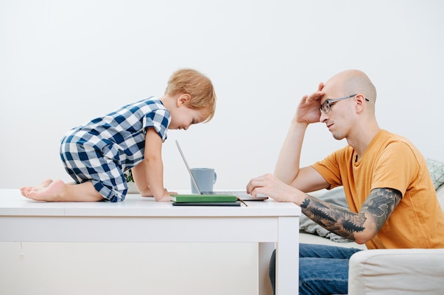 Ragazzo curioso del bambino che esamina il padre dello schermo che lavora al suo computer portatile