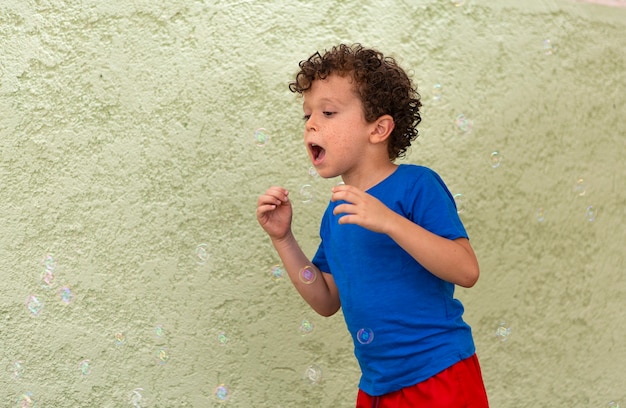 Ragazzo dai capelli ricci con le lentiggini che gioca in cortile con le bolle di sapone.