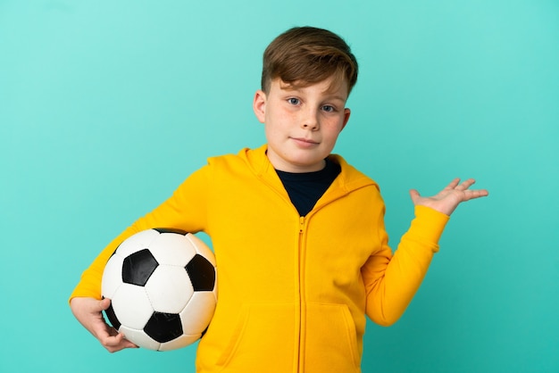 Ragazzo dai capelli rossi che gioca a calcio isolato su sfondo blu avendo dubbi mentre alza le mani