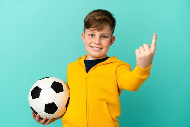 Ragazzo dai capelli rossi che gioca a calcio isolato su sfondo blu facendo un gesto imminente