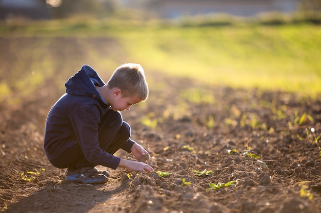 Ragazzo del bambino che accovaccia da solo nel campo vuoto