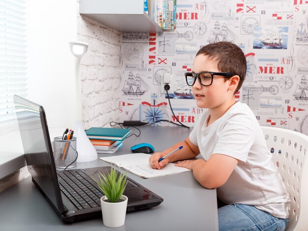 Ragazzo del bambino che fa i compiti al computer portatile sulla piattaforma online