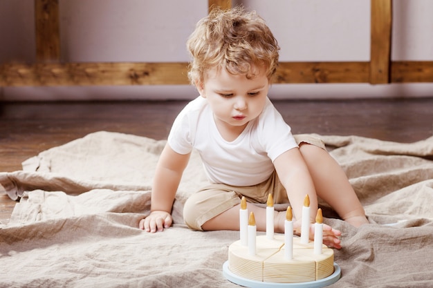 Ragazzo del bambino che gioca nella sua stanza con una torta giocattolo di legno