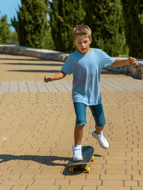 Ragazzo del bambino che impara a guidare lo skateboard nel parco. Modello di camicia