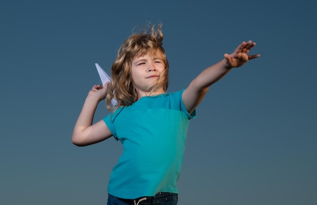 Ragazzo del bambino che lancia un aeroplano di carta con il fondo del cielo blu