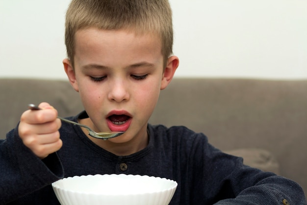 Ragazzo del bambino che mangia minestra da una ciotola con un cucchiaio