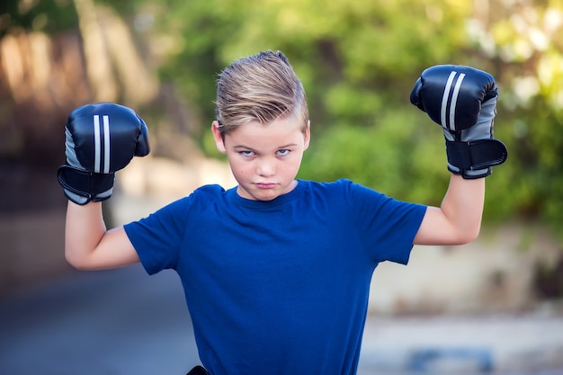 Ragazzo del bambino con i guantoni da boxe che mostrano forte all'aperto