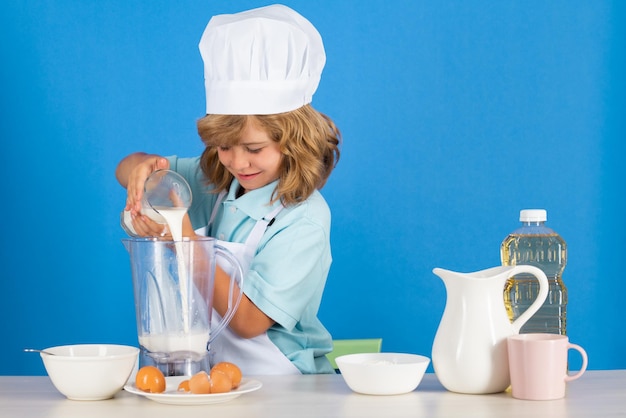 Ragazzo del bambino in cappello da cuoco e grembiule che cucina preparando il pasto piccolo cuoco con verdure in cucina naturale