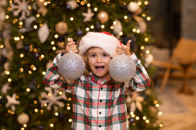 Ragazzo del bambino in cappello della Santa vicino all'albero di Natale a casa