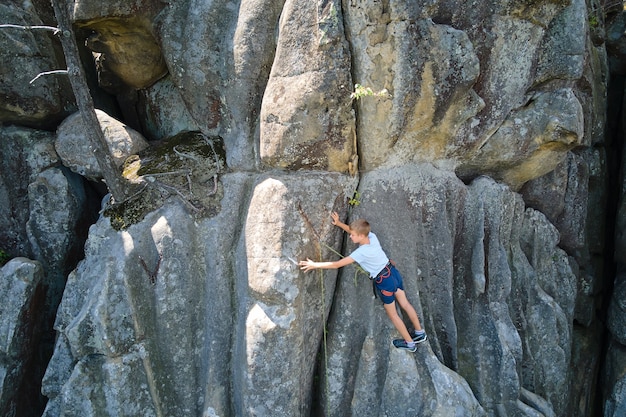 Ragazzo del bambino in giovane età che scala la parete ripida della montagna rocciosa. Lo scalatore del bambino supera il percorso impegnativo. Impegnarsi nel concetto di sport estremo.