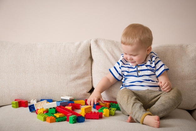 Ragazzo del bambino in una camicia a righe che gioca blocchi di plastica colorati sul divano all'interno bambino divertendosi