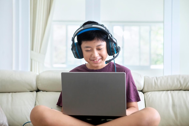 Ragazzo del preteen che utilizza un computer portatile e le cuffie a casa