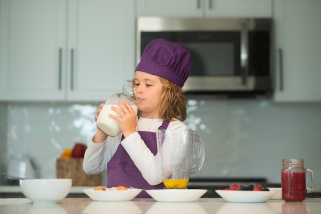 Ragazzo del ragazzo del cuoco unico di preparazione del cibo del bambino in grembiule e cappello del cuoco unico che cucina al cibo sano della cucina