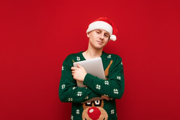 Ragazzo dell'adolescente del ritratto con il computer portatile della tenuta del maglione di Natale