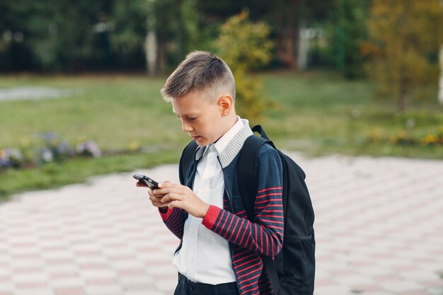 Ragazzo dell'adolescente dello scolaro con il telefono cellulare che sta alla via.