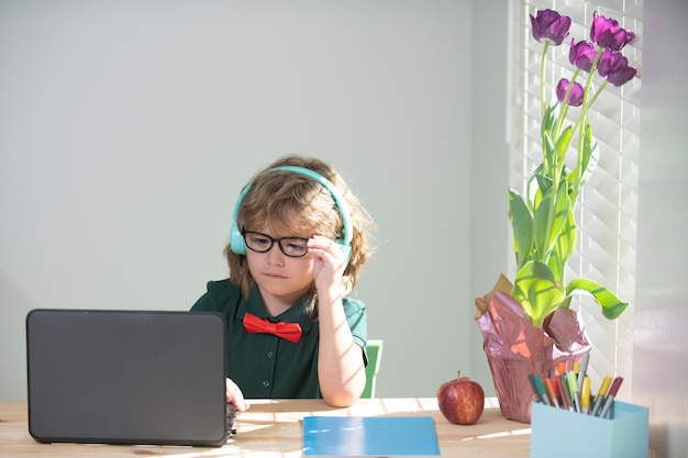 Ragazzo della scuola che fa i compiti con il bambino del computer portatile che usa i gadget per studiare l'istruzione e l'apprendimento a distanza