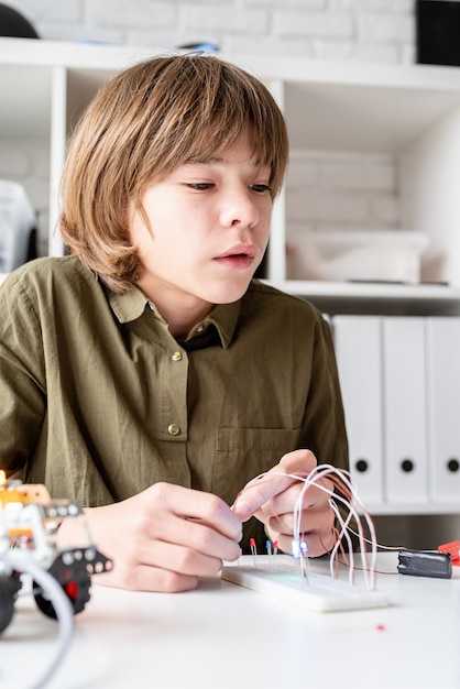 Ragazzo di 12 anni che costruisce un'automobile del robot che si siede al tavolo