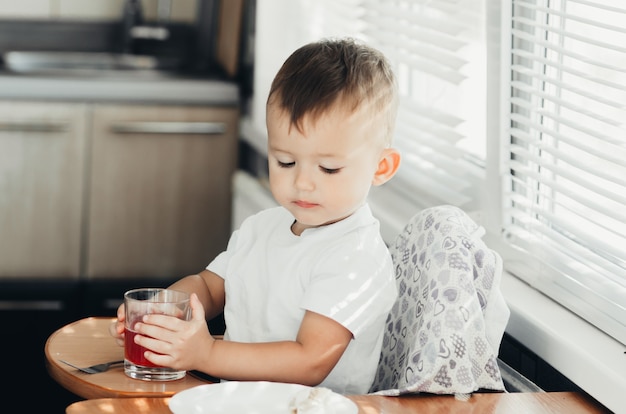 Ragazzo di due anni che beve succo da una tazza di vetro in cucina
