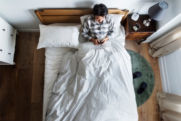 Ragazzo di etnia asiatica utilizzando il telefono sul letto