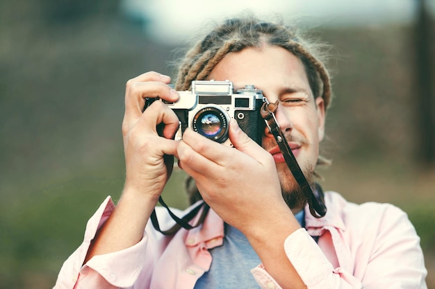 Ragazzo di fotografia con la barba bionda hipster con dreadlocks che scatta foto sulla posizione della natura nella vista all'aperto della foresta