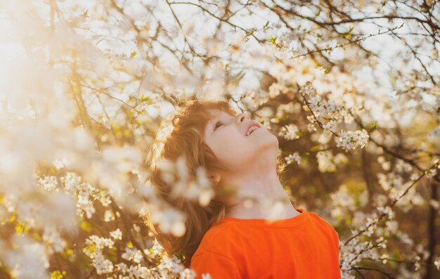 Ragazzo di primavera in un albero in fiore nel parco di primavera Bambino sorridente all'aperto Giardino in fiore