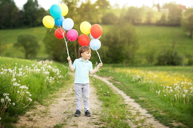 Ragazzo di quattro anni con palloncini cammina in un prato verde con denti di leone