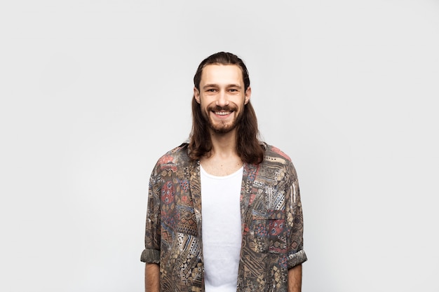 Ragazzo divertente amichevole sorridente, hippy attraente e gentile. Uomo spensierato alla moda del viaggiatore dei pantaloni a vita bassa su un fondo bianco dello studio, stile di vita della gente