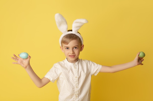 Ragazzo divertente bambino felice con uova di Pasqua e orecchie da coniglio su sfondo giallo