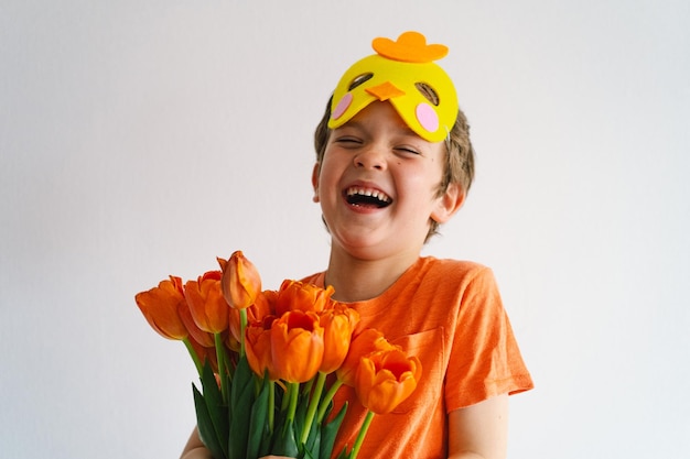 Ragazzo divertente con tulipani arancioni e nella maschera di un pulcino su sfondo bianco