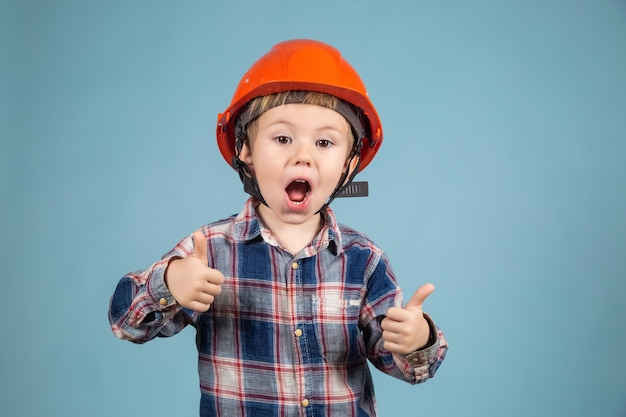 Ragazzo divertente ingegnere o architetto con un casco arancione protettivo che mostra il pollice in su