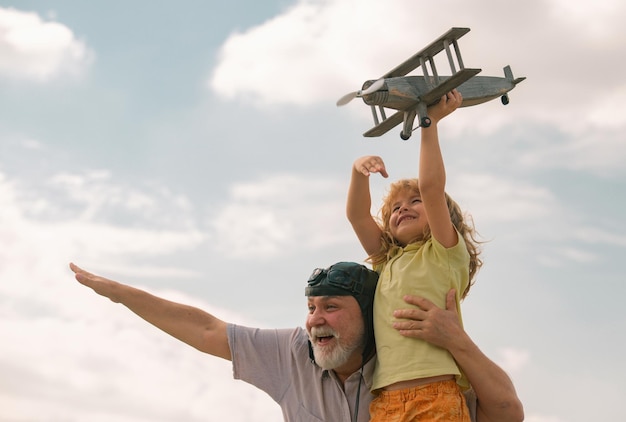 Ragazzo e nonno eccitati del bambino che si divertono con l'aereo all'aperto sul fondo del cielo con lo spazio della copia ch