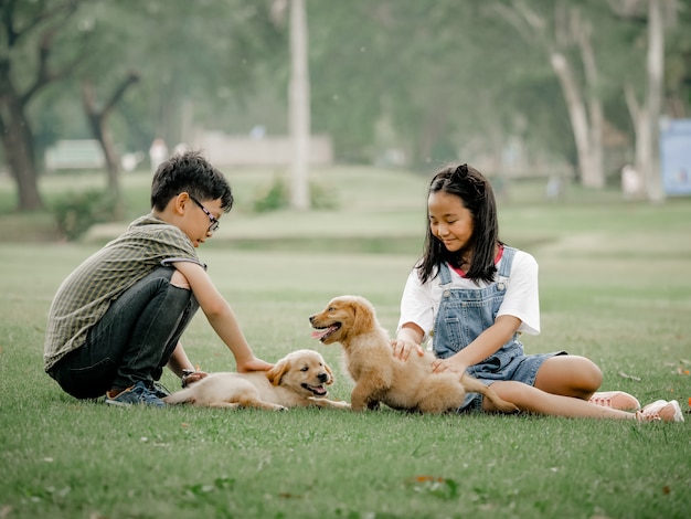 Ragazzo e ragazza asiatici che giocano il cucciolo di cane del wiyh in parco