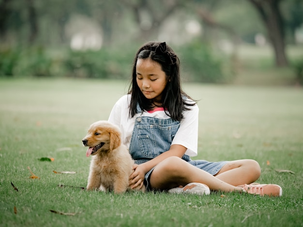 Ragazzo e ragazza asiatici che giocano il cucciolo di cane del wiyh in parco