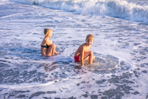 Ragazzo e ragazza che giocano sulla spiaggia durante le vacanze estive. Bambini in natura con bel mare, sabbia e cielo blu.
