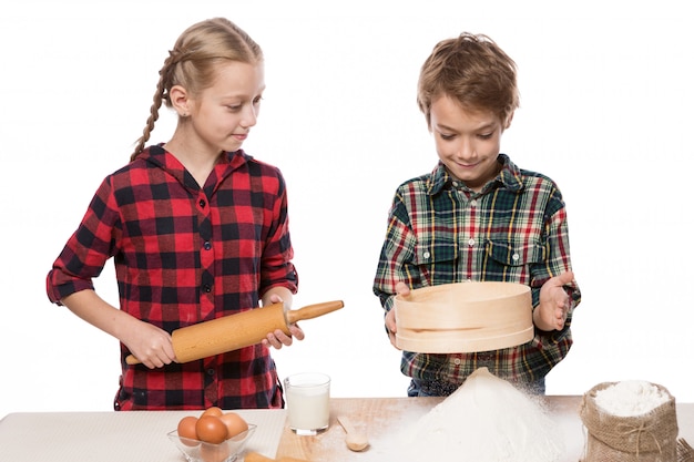 Ragazzo e ragazza che producono pasta per cottura, fratello e sorella, ragazzo che setaccia farina, ragazza che guarda, su fondo bianco, isolato