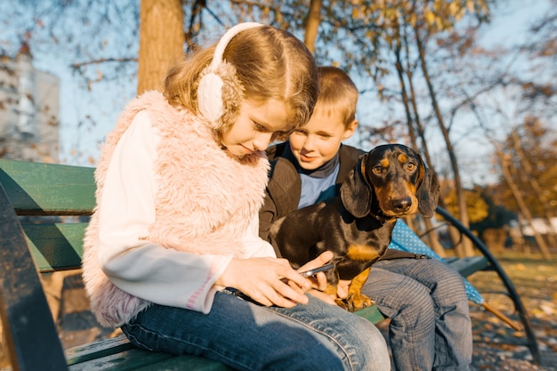 Ragazzo e ragazza che si siedono sul banco nel parco con il cane