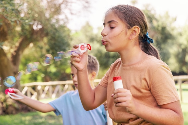 Ragazzo e ragazza che soffiano bolle di sapone in un parco