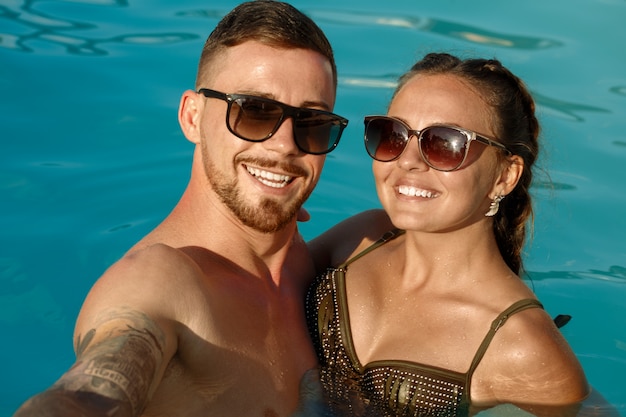 Ragazzo e ragazza felici che prendono selfie mentre riposando nella piscina