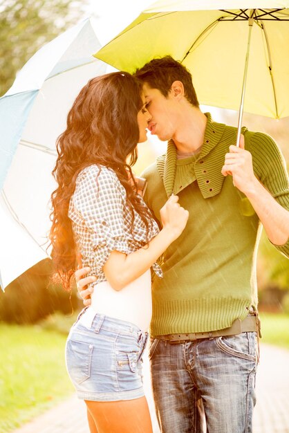 Ragazzo e ragazza in piedi che si abbracciano sotto gli ombrelloni e si baciano.